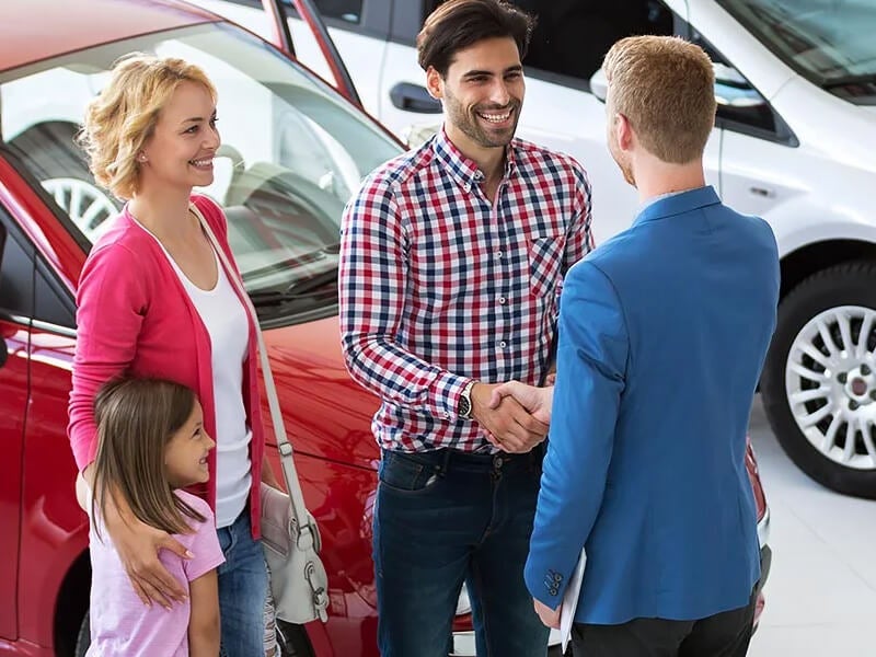 family in car dealership, man shaking hands with salesman