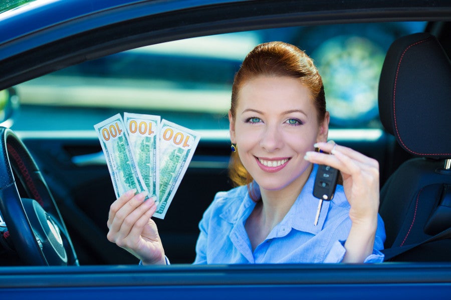woman in car holding up cash and car key